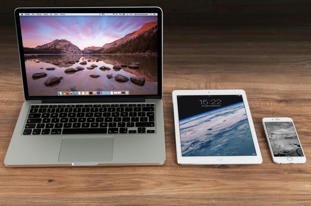 Best Spot the Difference Books. Apple laptop, tablet, and smartphone neatly arranged on a wooden desk, displaying scenic and space-themed screens.